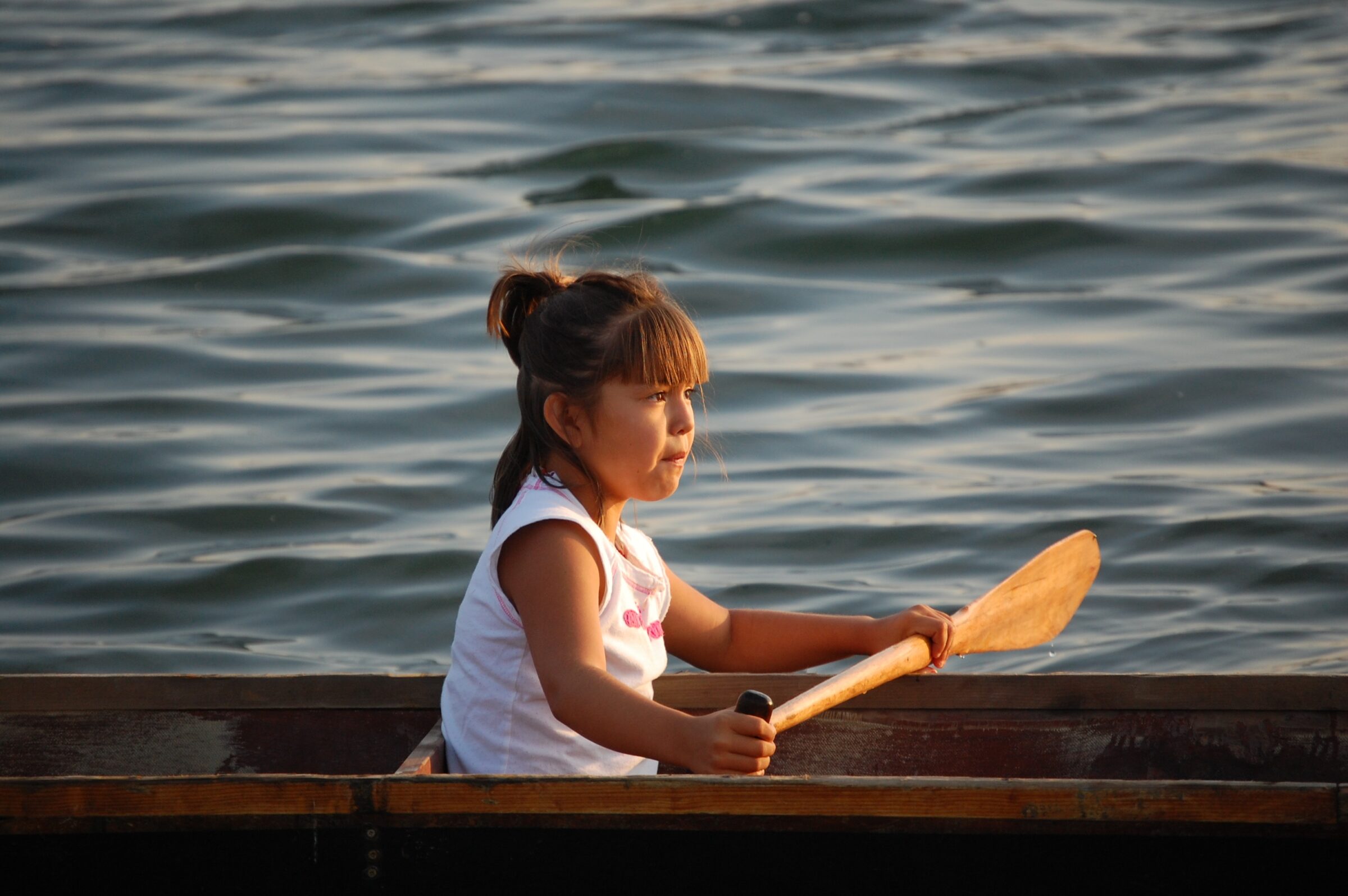 A young girl sits in a canoe holding a paddle